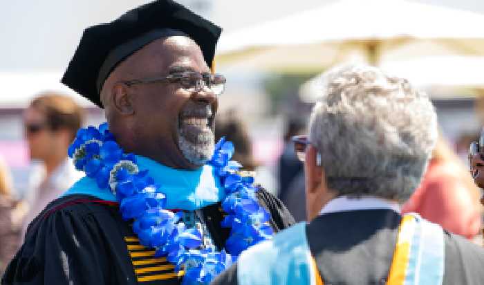 A man wearing graduation regalia associated with the Ed.D. degree smiles while standing next to another person.