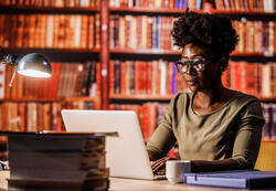 Young woman using laptop, sitting at desk in a library.