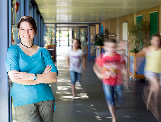 Portrait of a smiling elementary school teacher with running children in the school corridor
