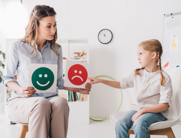 adult psychologist showing happy and sad emotion faces cards to child