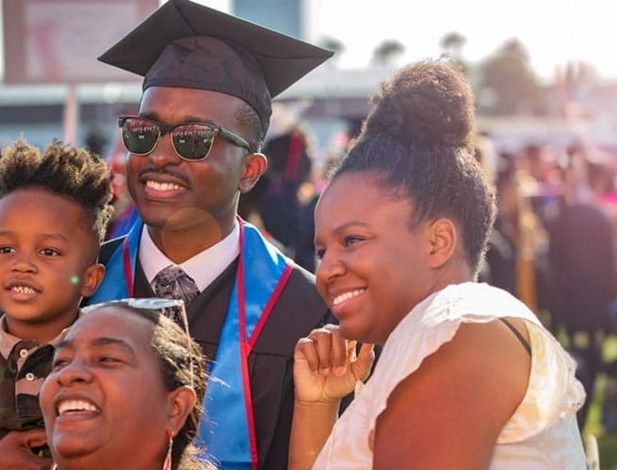 male UMass Global graduate at commencement taking a selfie with his family
