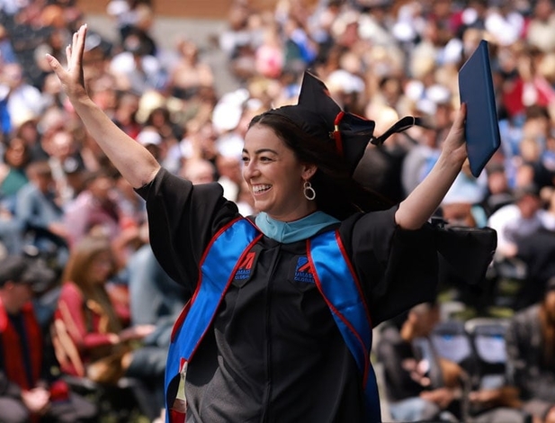 female graduate from UMass Global at commencement and waiving at crowd