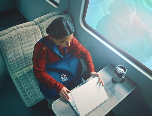 A young woman sitting on a train and opening her laptop.